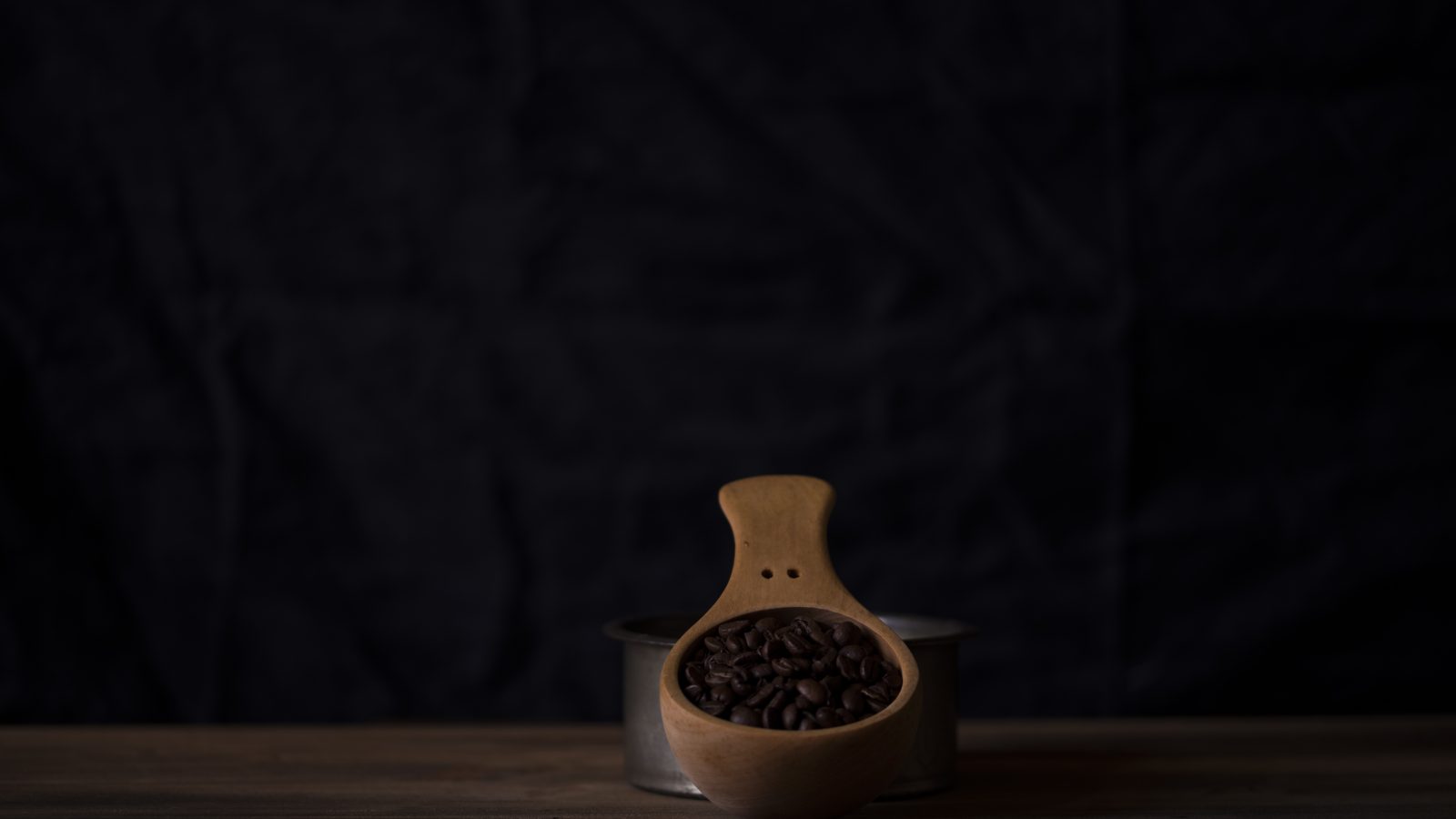 Dark roasted coffee beans in a wooden scoop against a dark backdrop, representing Boa Vista Natural