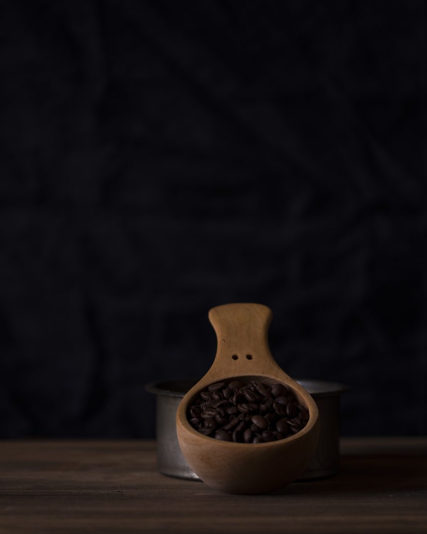 Dark roasted coffee beans in a wooden scoop against a dark backdrop, representing Boa Vista Natural