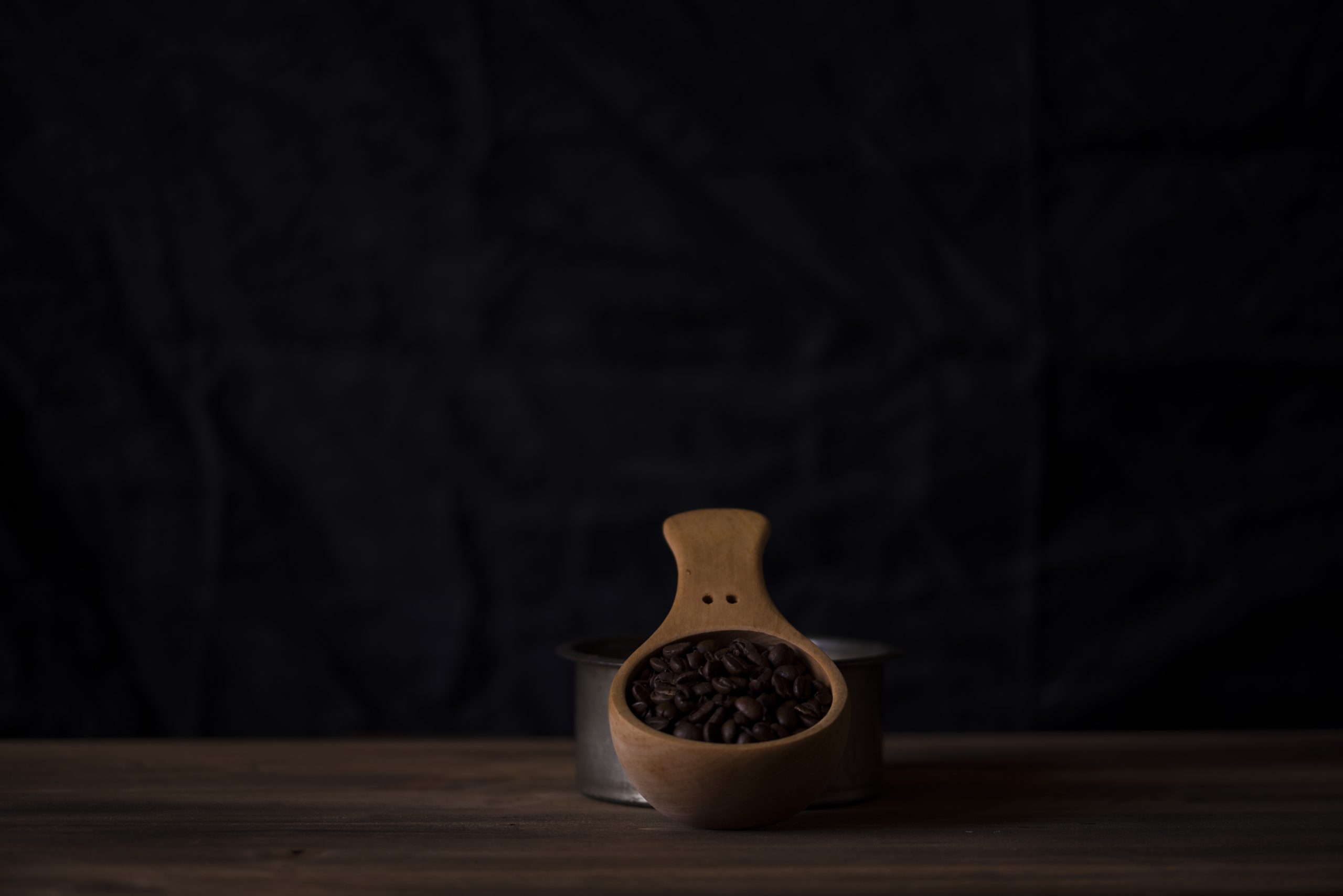 Dark roasted coffee beans in a wooden scoop against a dark backdrop, representing Boa Vista Natural