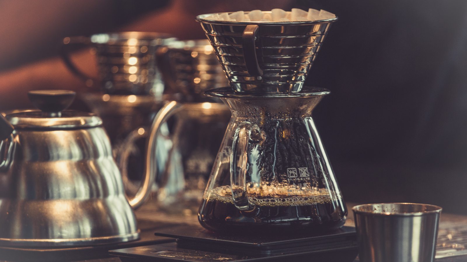 Warm pour-over coffee brewing scene with glass carafes and a gooseneck kettle, representing El Cielo Antigua