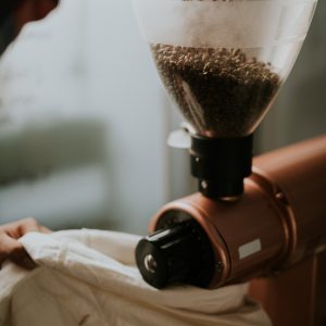 Electric single-dose grinder with copper-toned body pouring beans into the hopper