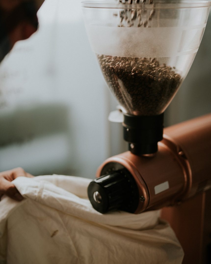 Electric single-dose grinder with copper-toned body pouring beans into the hopper
