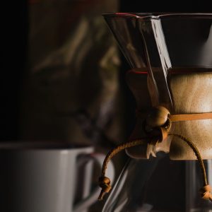 Hourglass-shaped glass carafe with wood collar and leather tie, filled with brewed coffee