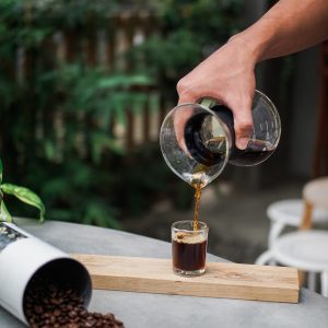 Hand pouring steeped coffee from a glass brewing vessel into a small glass