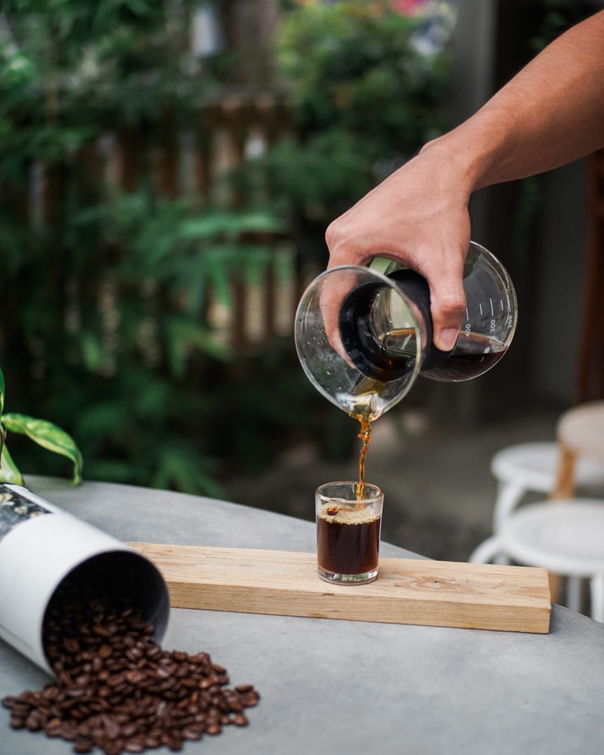 Hand pouring steeped coffee from a glass brewing vessel into a small glass