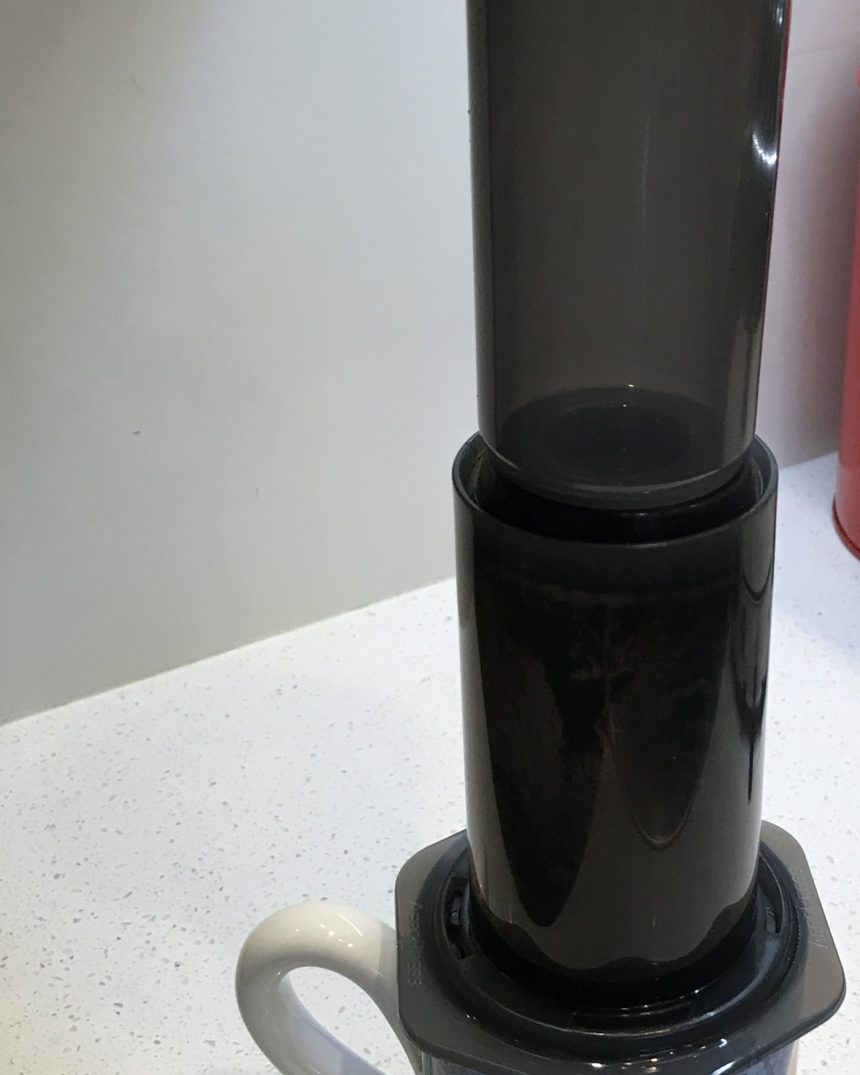 Plunger-style immersion coffee press seated on a mug