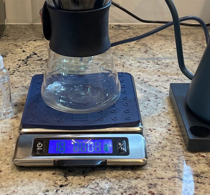 Gooseneck kettle beside a pour-over dripper and carafe resting on a digital coffee scale